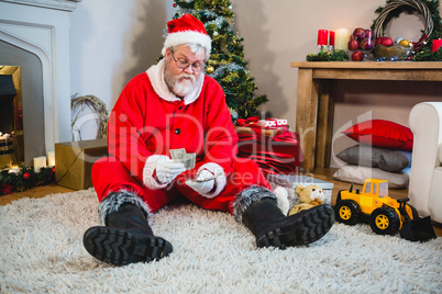 Santa claus sitting on the floor and counting cash