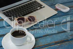 Laptop, black coffee, sunglasses and mouse on wooden plank