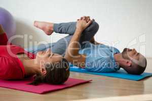 Instructor and student exercising while lying on mat in yoga studio