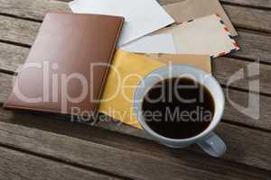 Coffee with various envelopes and diary on wooden plank