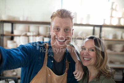 Happy male and female potter standing together in pottery workshop