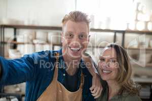 Happy male and female potter standing together in pottery workshop