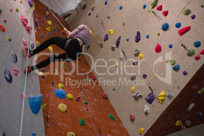 Female athlete climbing wall with rope in gym