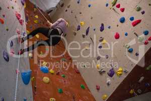 Female athlete climbing wall with rope in gym