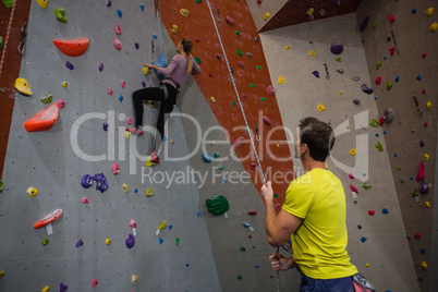 Man holding rope looking at athlete climbing wall in fitness studio