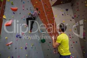 Man holding rope looking at athlete climbing wall in fitness studio