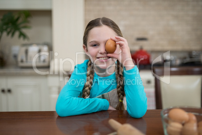 Girl holding egg while sitting on table in the kitchen