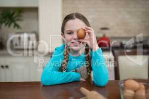 Girl holding egg while sitting on table in the kitchen