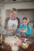 Smiling mother and daughter preparing cookies in kitchen