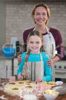 Smiling mother and daughter preparing cookies in kitchen