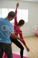 Yoga instructor assisting student in exercising at health club