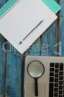 Blank book, pen, magnifying glass and laptop on wooden plank