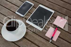 Black coffee, mobile phone, digital tablet, pen and sticky note on wooden plank