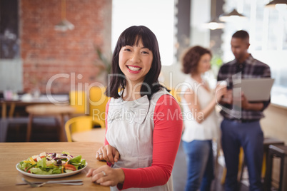 Portrait of smiling woman sitting with fresh salad at coffee shop