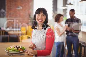 Portrait of smiling woman sitting with fresh salad at coffee shop