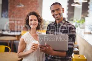 Smiling young friends standing with disposable coffee cup and laptop