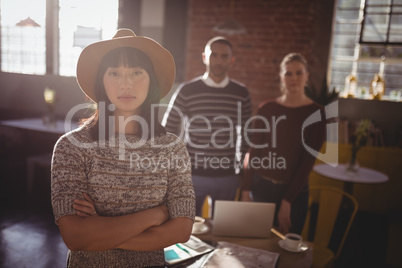 Portrait of woman standing with arms crossed against colleagues