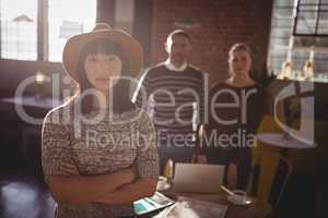 Portrait of woman standing with arms crossed against colleagues