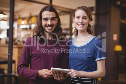 Portrait of confident young waitress and man holding digital tablet