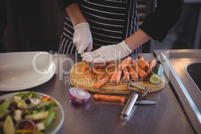 Midsection of female chef cutting carrots on board in kitchen