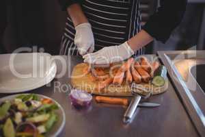 Midsection of female chef cutting carrots on board in kitchen