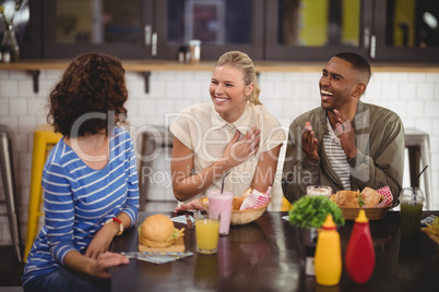 Cheerful young friends talking while sitting with food and drink at coffee shop