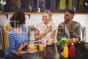 Cheerful young friends talking while sitting with food and drink at coffee shop