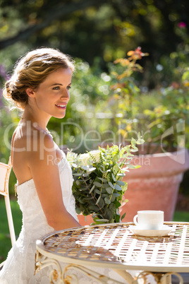 Smiling bride holding bouquet looking away while sitting on chair