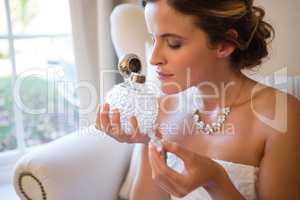 Beautiful bride smelling perfume while sitting on armchair