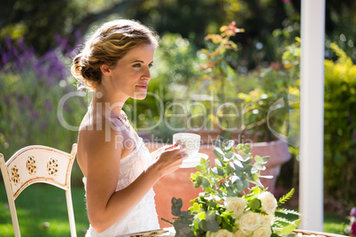 Beautiful bride having coffee while sitting on chair in yard