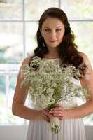 Portrait of beautiful bride holding bouquet while standing at home