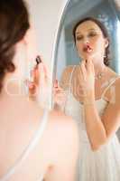 Rear view of beautiful bride applying lip gloss reflecting on mirror