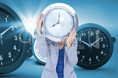 Composite image of businesswoman holding clock in front of face