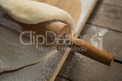 Cropped image of rolling pin on rolled dough over cutting board