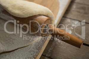 Cropped image of rolling pin on rolled dough over cutting board
