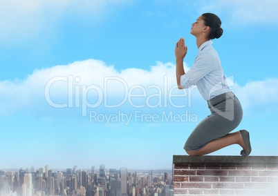 Businesswoman praying on brick rooftop over city