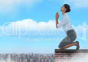 Businesswoman praying on brick rooftop over city