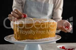 Woman toping a fresh baked cake with cherry
