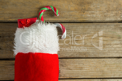 Wrapped gift box and candy cane in stocking against wooden wall