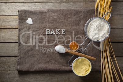 Wheat stem, wear flour, sieve, spoon placed over a cloth on wooden table