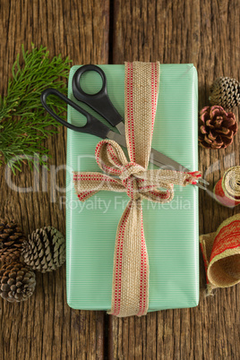 Scissors, pine cones, leaves and ribbon with wrapped gift box on wooden table
