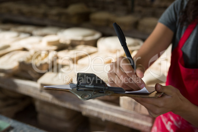 Female potter writing in clipboard