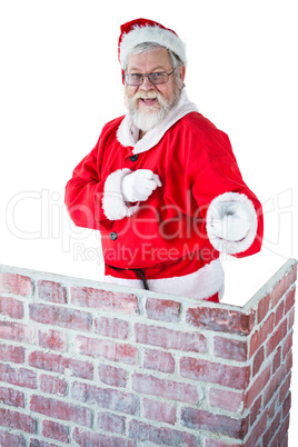 Santa claus standing behind the chimney and pointing against white background