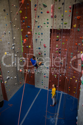 Male trainer hanging on rope talking to woman at health club