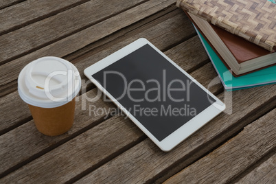 Disposable glass, books and digital tablet on wooden plank