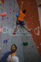 Woman with rope looking at man climbing wall in health club