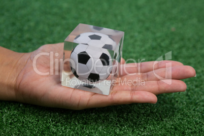 Hand holding acrylic football cube on artificial grass