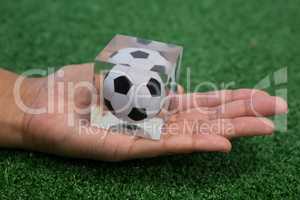 Hand holding acrylic football cube on artificial grass
