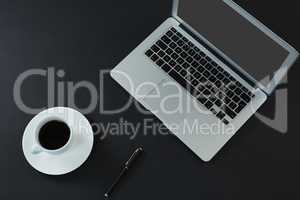 Laptop, pen and black coffee on black background