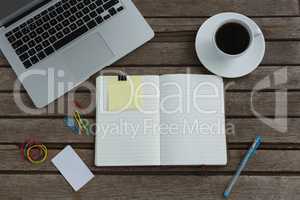 Black coffee, laptop, organizer and stationery on wooden plank